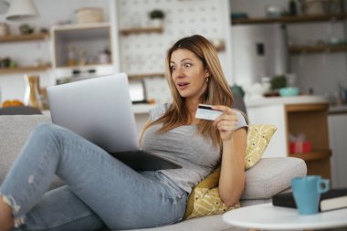 Evde kredi kartını ve laptopunu kullanan genç bir kadın. Güzel bir kadın internetten alıyor..
