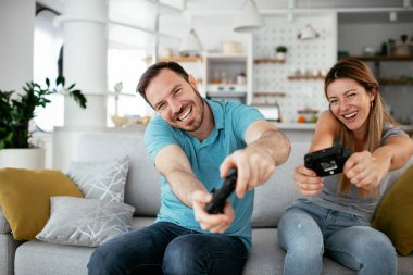 Karı koca oturma odasında joysticklerle oyun oynuyorlar. Sevgili çift evde video oyunu oynuyor..