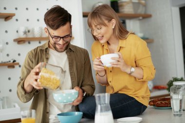Genç çift evde kahvaltı hazırlıyor. Sevgi dolu çift mutfakta mısır gevreği yiyor..