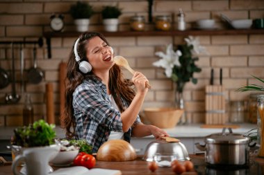 Sevimli, sevimli, neşeli, güzel, modaya uygun, modaya uygun, mutfakta müzik dinleyen kız. Mutfakta şarkı söyleyen genç mutlu kadın.