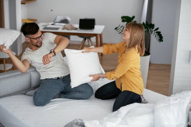 Erkek arkadaş ve kız arkadaş yatakta yastık kavgası yapıyor. Mutlu çift evde eğleniyor.