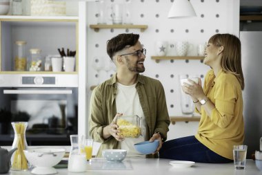 Genç çift evde kahvaltı hazırlıyor. Sevgi dolu çift mutfakta mısır gevreği yiyor..
