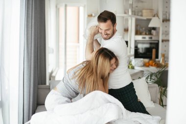 Çift evde eğleniyor, yastıklarla kavga ediyor.