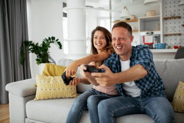 Erkek arkadaşı ve kız arkadaşı oturma odasında joysticklerle oyun oynuyorlar. Sevgili çift evde video oyunu oynuyor..