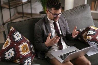 Evde pantolonsuz çalışan bir iş adamı. Genç adam video görüşmesi sırasında bilgisayarı kullanıyor..