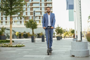 Genç yakışıklı işadamı sokakta elektrikli scooter kullanıyor.