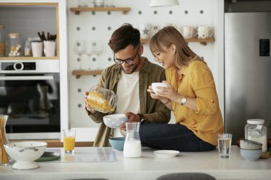 Genç çift evde kahvaltı hazırlıyor. Sevgi dolu çift mutfakta mısır gevreği yiyor..