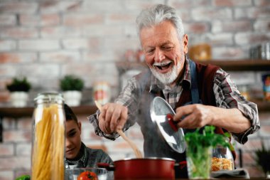 Büyükbaba ve torun oynuyor. Yaşlı adam torunuyla mutfakta yemek pişiriyor..