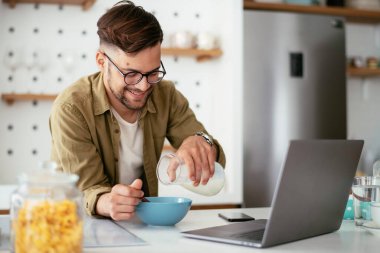 Genç adam kahvaltı yapıyor ve internette haberleri okuyor. Yakışıklı adam evde eğleniyor..