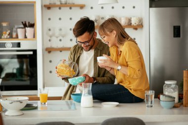 Genç çift evde kahvaltı hazırlıyor. Sevgi dolu çift mutfakta mısır gevreği yiyor..