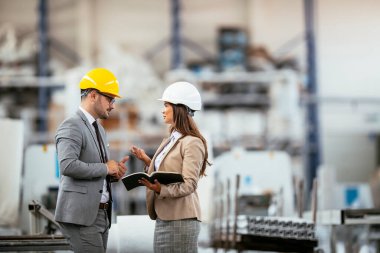 İşadamı ve iş kadını fabrikada iş konuşuyorlar.