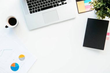 Ofis masasının en üst görüntüsü. Laptop, kahve ve malzeme dolu beyaz ofis masası..