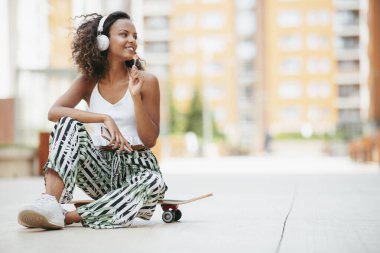 Genç Afrikalı bir kadın. Güzel bir kadın kaykayın üzerinde oturmuş müzik dinliyor..
