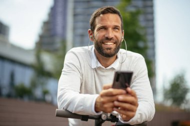 Kulaklıkla müzik dinleyen, elektrikli scooter kullanan genç adamın yakın görüntüsü.