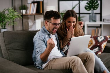 Evde dizüstü bilgisayar başında film ya da televizyon izleyen mutlu genç çift.