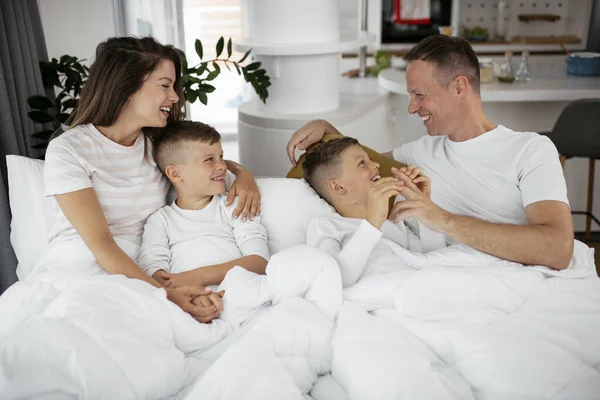 Genç bir aile yatakta eğleniyor. Oğulları yatakta dinlenen mutlu ebeveynler..