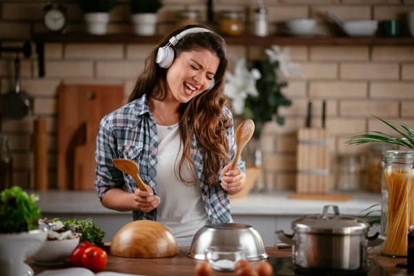Sevimli, sevimli, neşeli, güzel, modaya uygun, modaya uygun, mutfakta müzik dinleyen kız. Mutfakta şarkı söyleyen genç mutlu kadın.