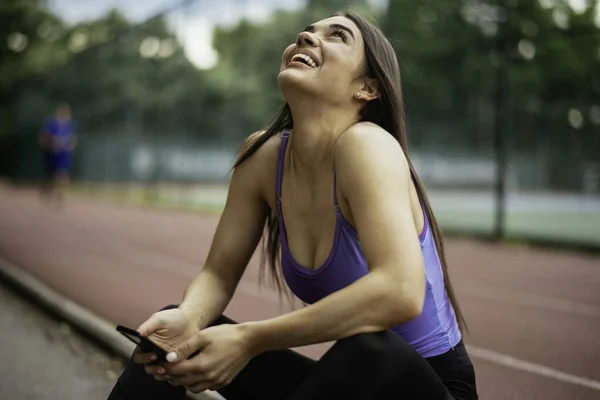 漂亮的女人从锻炼中休息 年轻女运动员坐在长椅上 用电话 — 图库照片