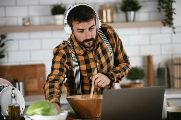 Portrait of handsome man in kitchen. Young man cooking while using laptop.