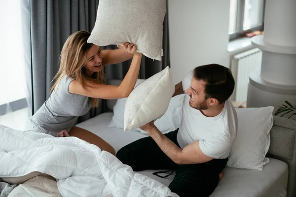 Young couple fighting pillows on the bed. Happy couple having fun at home