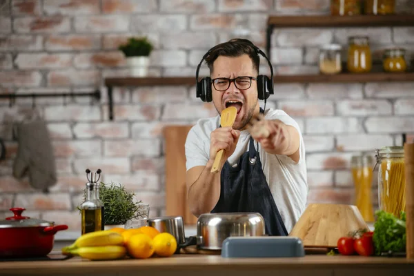 Happy man in earphones listening to music and dancing while cooking in kitchen.