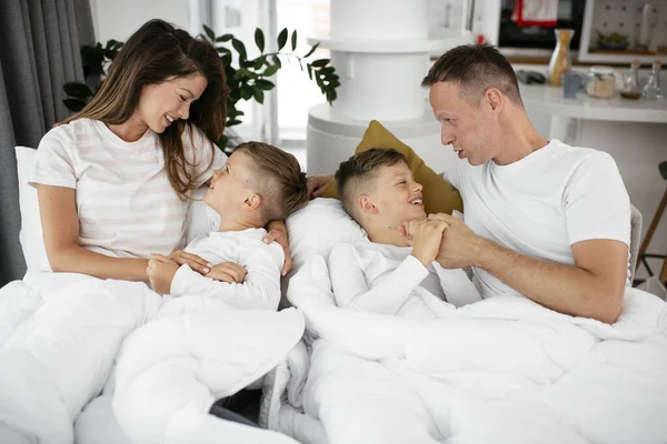 Genç bir aile yatakta eğleniyor. Oğulları yatakta dinlenen mutlu ebeveynler..