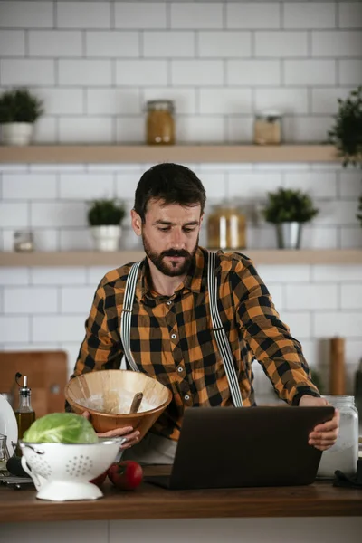 Portrait of handsome man in kitchen. Young man cooking while having video call.