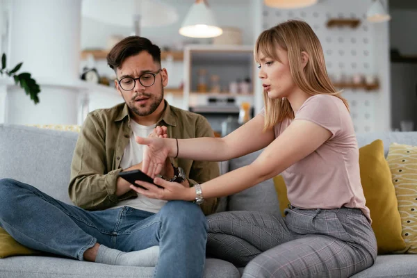 Husband and wife are arguing on the couch. Angry wife is yelling at her husband