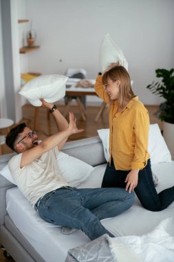 Erkek arkadaş ve kız arkadaş yatakta yastık kavgası yapıyor. Mutlu çift evde eğleniyor.