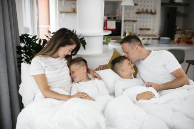 Genç bir aile yatakta eğleniyor. Oğulları yatakta dinlenen mutlu ebeveynler.