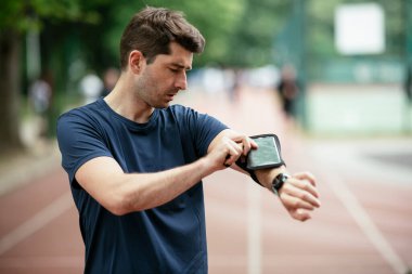 Genç adam antrenman sırasında kalp atışlarını kontrol ediyor. Genç adam atletizm pistinde egzersiz yapıyor..