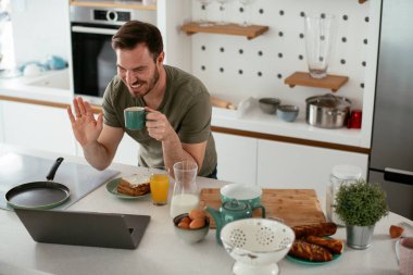 Mutfakta kahve içen yakışıklı adam. Genç adam video görüşmesi yapıyor..