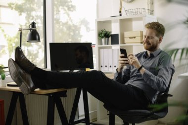 Ofiste akıllı telefon kullanan kızıl saçlı yakışıklı bir iş adamı.