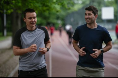 Gençler yarış pistinde antrenman yapıyor. İki genç arkadaş atletizm pistinde koşuyor.