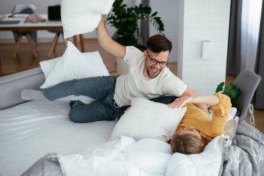 Erkek arkadaş ve kız arkadaş yatakta yastık kavgası yapıyor. Mutlu çift evde eğleniyor.