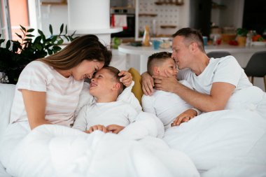 Genç bir aile yatakta eğleniyor. Oğulları yatakta dinlenen mutlu ebeveynler.
