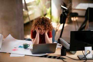 Yorgun ve güzel iş kadını proje üzerinde çalışıyor. Ofiste kıvırcık saçlı genç bir kadın var..