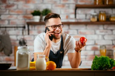 Yakışıklı adam mutfakta yemek pişiriyor ve cep telefonuyla konuşuyor..
