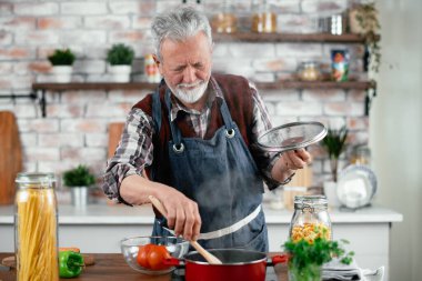 Yaşlı adam yemek yapıyor. Mutfakta kıdemli adam var..