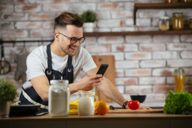 Yakışıklı adam mutfakta yemek pişiriyor ve cep telefonuyla konuşuyor..