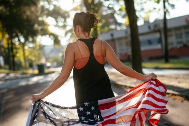 Amerikan bayrağı taşıyan güzel bir kadın. Koşu pistinde elinde Amerikan bayrağı olan genç bir kadının portresi.