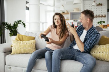 Karı koca oturma odasında joysticklerle oyun oynuyorlar. Sevgili çift evde video oyunu oynuyor..