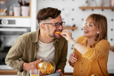 Genç çift evde kahvaltı hazırlıyor. Sevgi dolu çift mutfakta mısır gevreği yiyor..