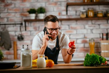Yakışıklı adam mutfakta yemek pişiriyor ve cep telefonuyla konuşuyor..