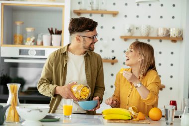 Genç çift evde kahvaltı hazırlıyor. Sevgi dolu çift mutfakta mısır gevreği yiyor..