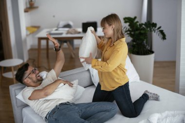 Erkek arkadaş ve kız arkadaş yatakta yastık kavgası yapıyor. Mutlu çift evde eğleniyor.