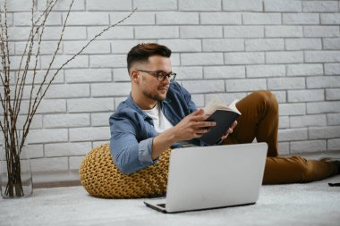 Genç yakışıklı adam yerde oturuyor ve kitabı okuyor..