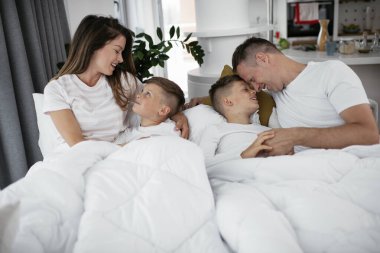 Genç bir aile yatakta eğleniyor. Oğulları yatakta dinlenen mutlu ebeveynler.