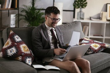 Evde pantolonsuz çalışan bir iş adamı. Genç adam video görüşmesi sırasında bilgisayarı kullanıyor..