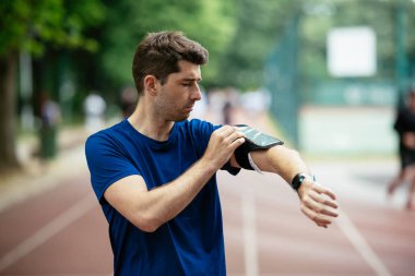 Genç adam antrenman sırasında kalp atışlarını kontrol ediyor. Genç adam atletizm pistinde egzersiz yapıyor..